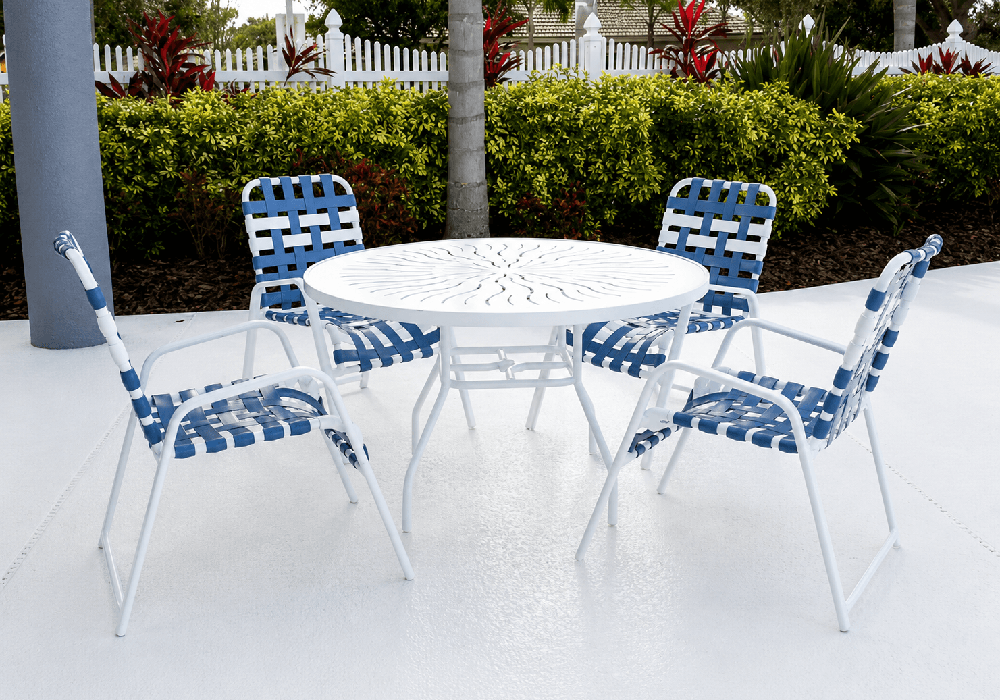 Resort-inspired outdoor dining set with woven vinyl strap chairs and a punch top design round aluminum table on a luxury pool deck.